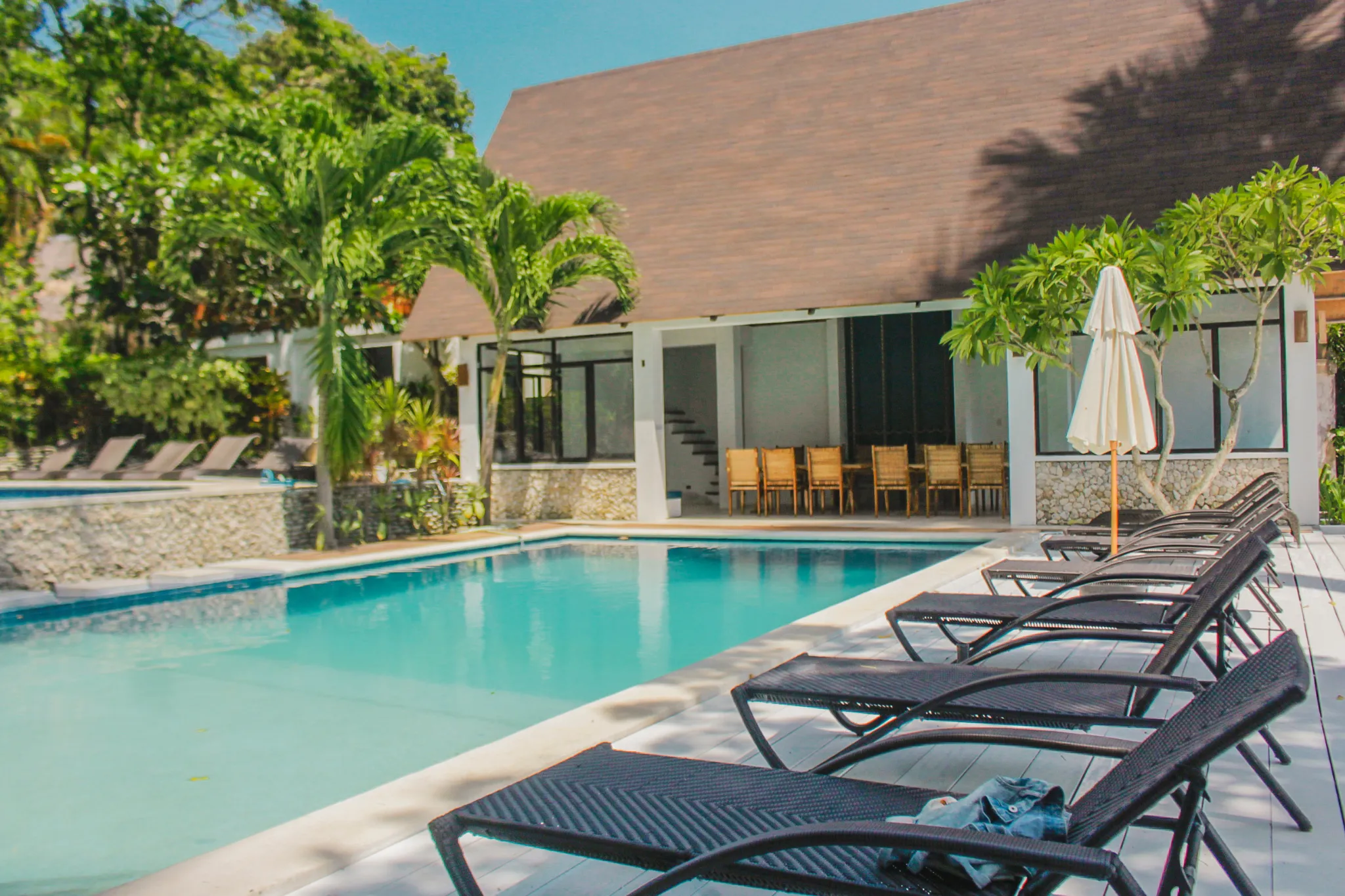 Serene poolside setting with black sun loungers, palm trees, and an open-air dining area at Casalay Boutique Villas & Dive Resort in Puerto Galera.